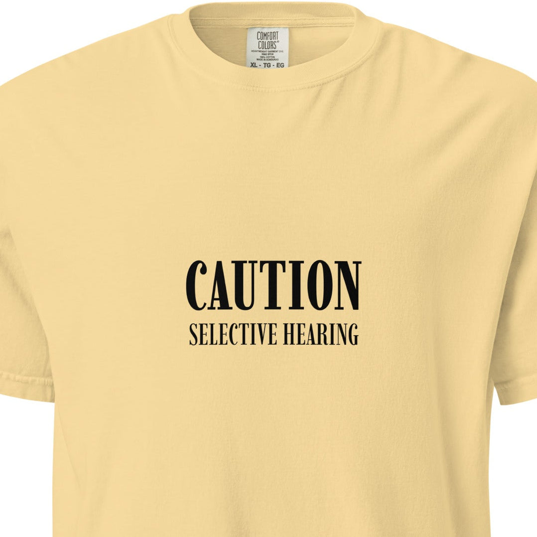 Unisex garment-dyed heavyweight T-shirt with caution: selective hearing print on butter-colored fabric, casual streetwear style.